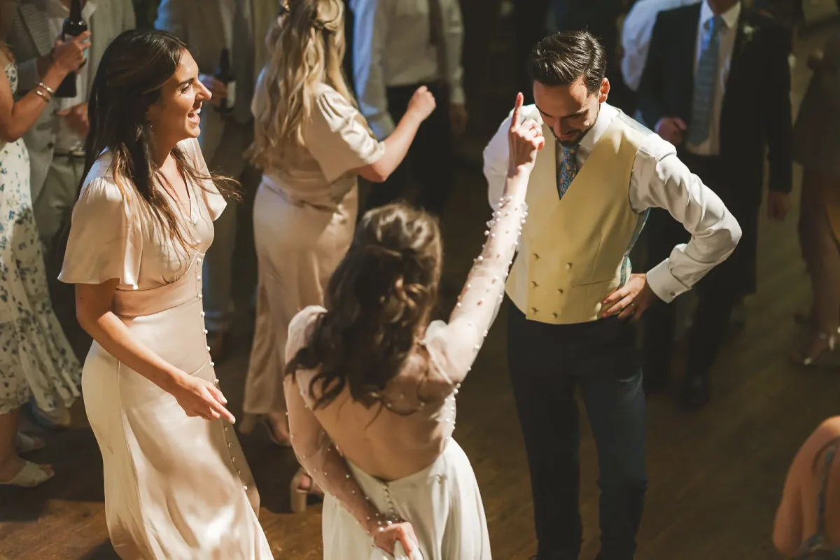 Bride dancing with the groom and bridesmaid on the dancefloor during the lively evening party in the tithe barn at Hinton St Mary Estate