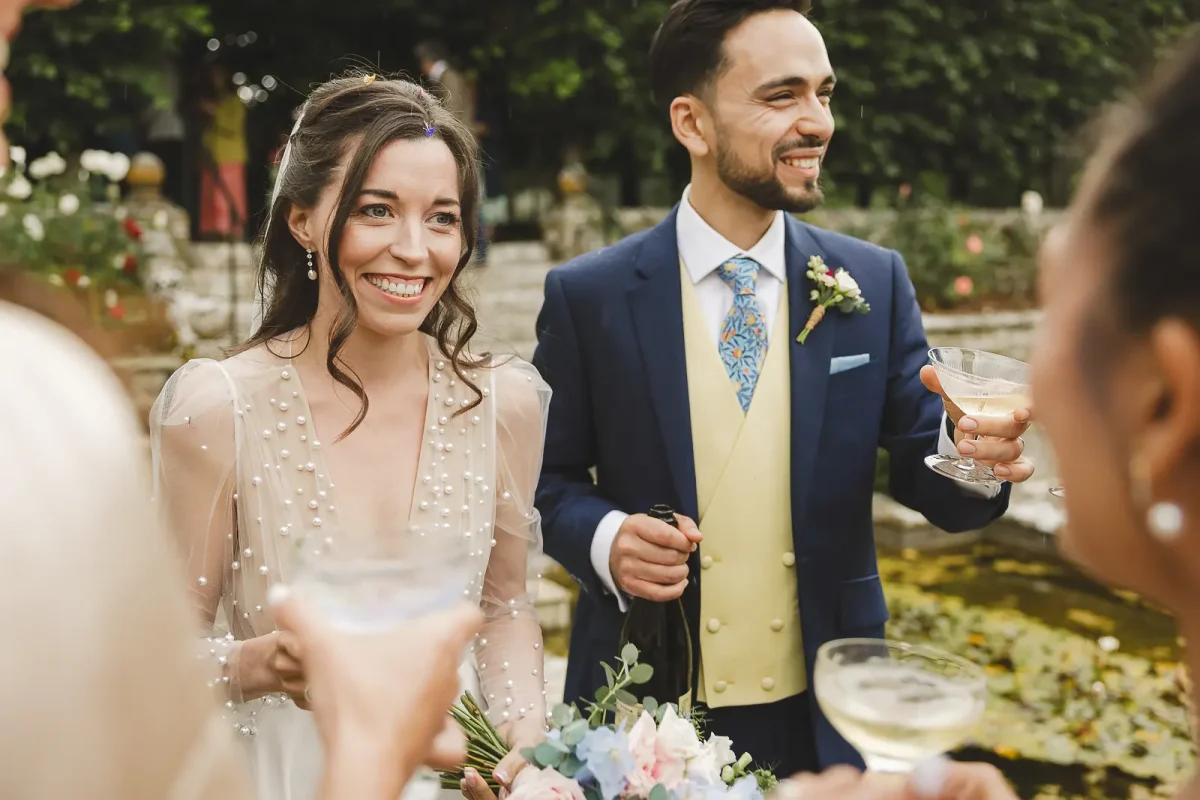 Bride and groom smiling and holding drinks during the drinks reception in the sunken garden at Hinton St Mary Estate