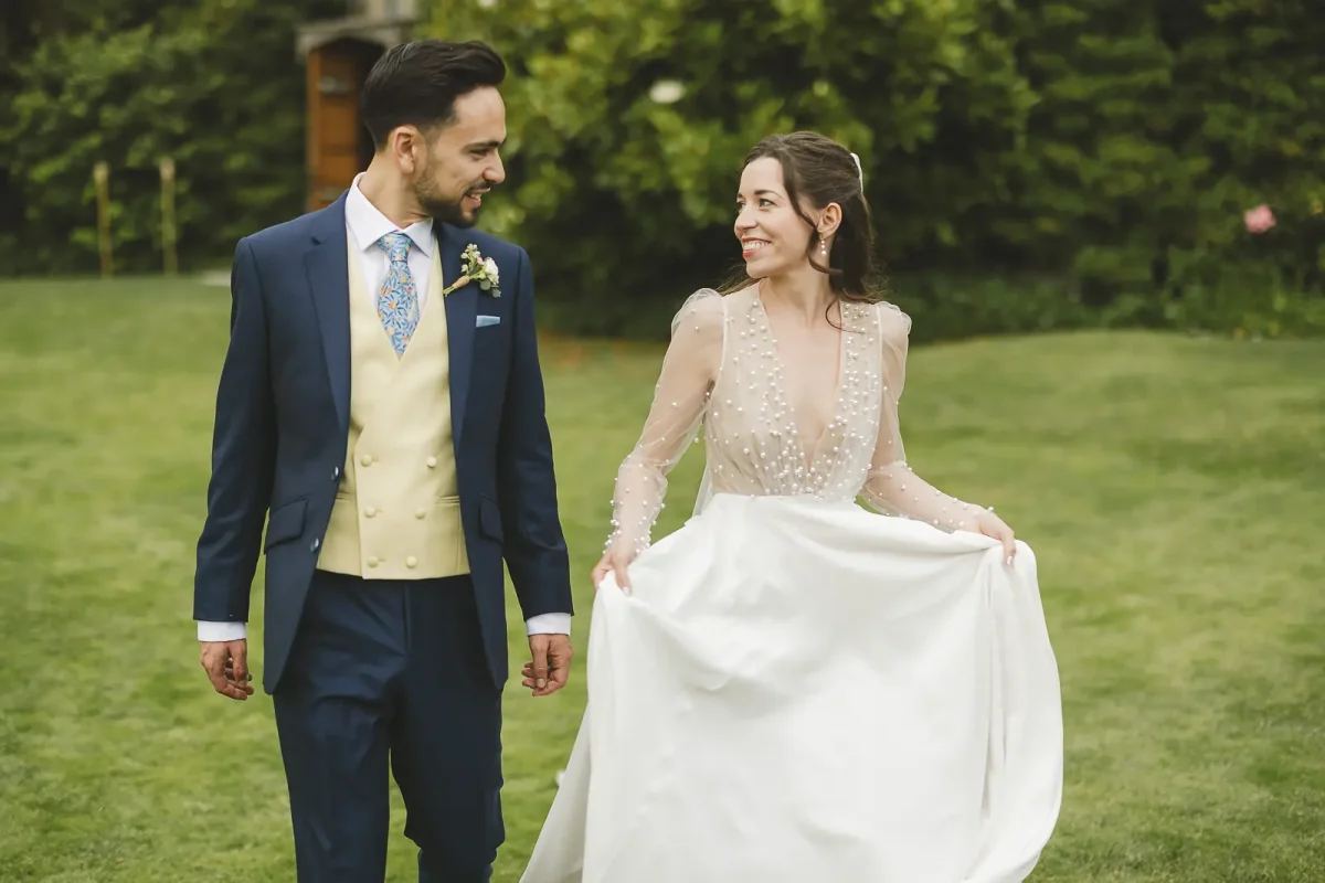 Bride lifting her dress skirt and laughing as she walks with her groom through the estate gardens at Hinton St Mary Estate