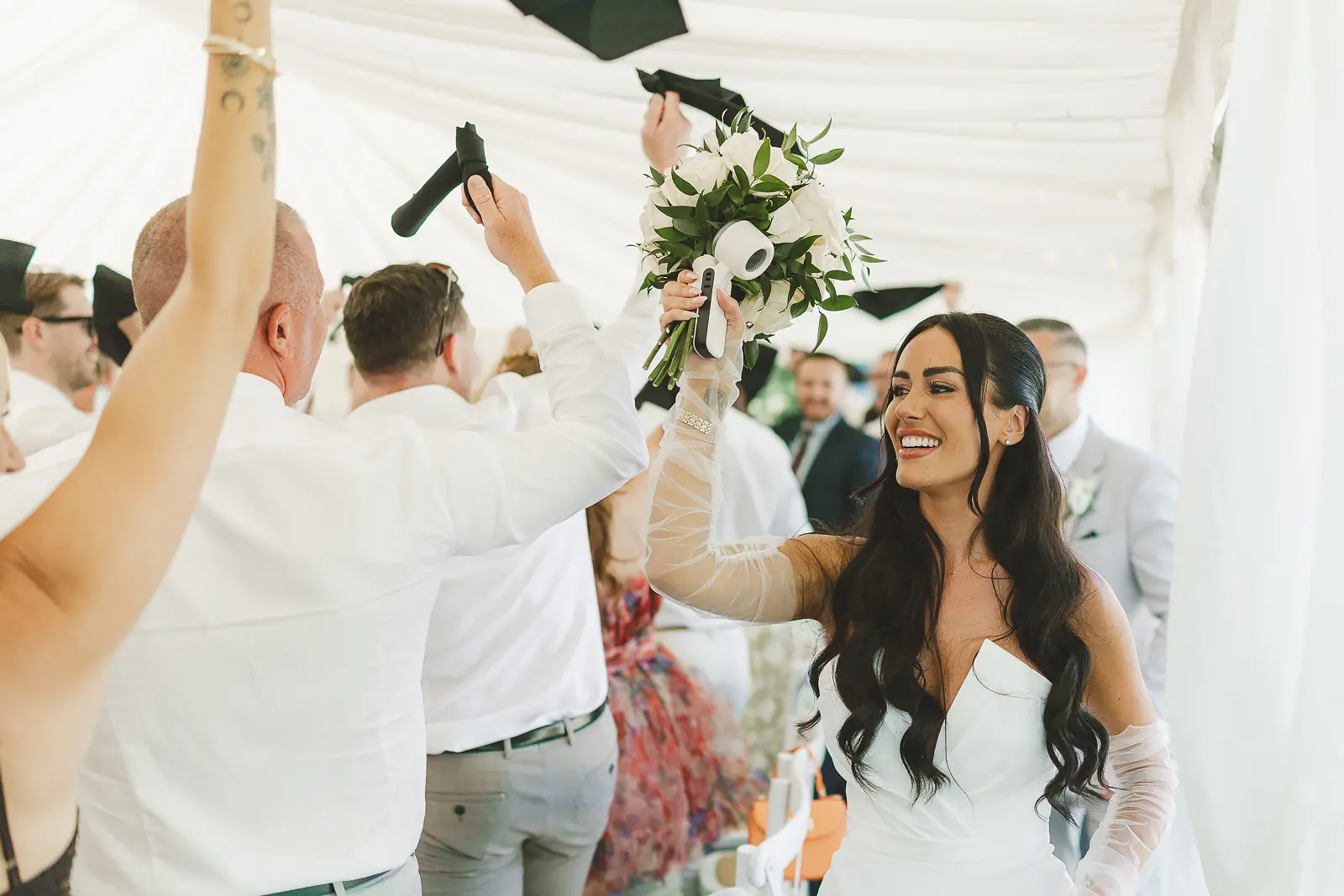 Bride walking back up the aisle after the ceremony as cheering guests look on from the marquee, joyful recessional moment