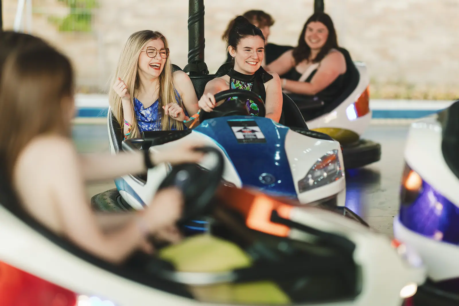 Guests in evening wear laughing on bumper cars at the May Ball fairground attraction