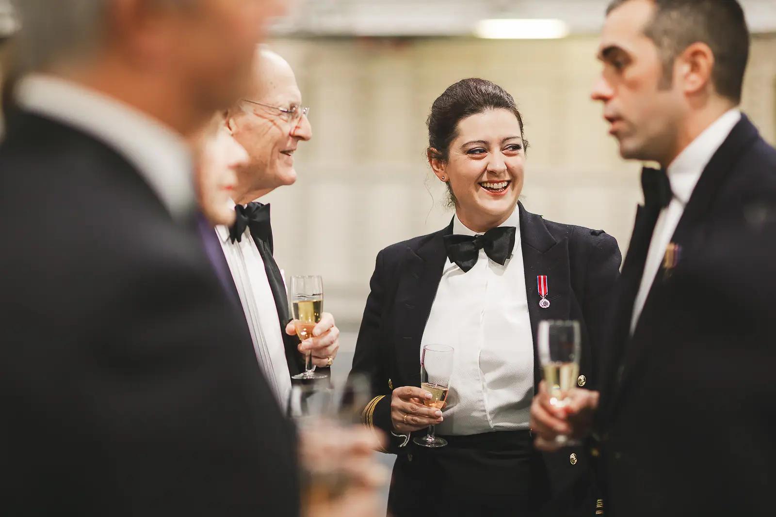 Female officer in uniform laughing with guests during champagne reception, candid reportage event photography