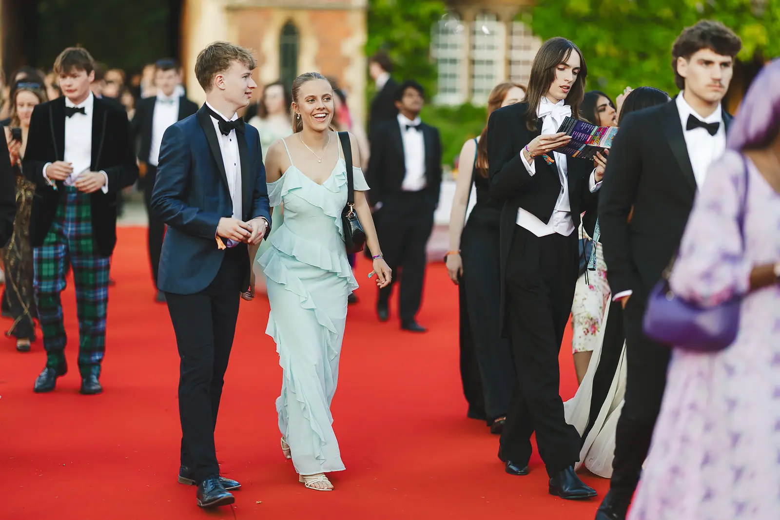 Couple in evening dress laughing as they walk the red carpet entrance at a Cambridge summer ball