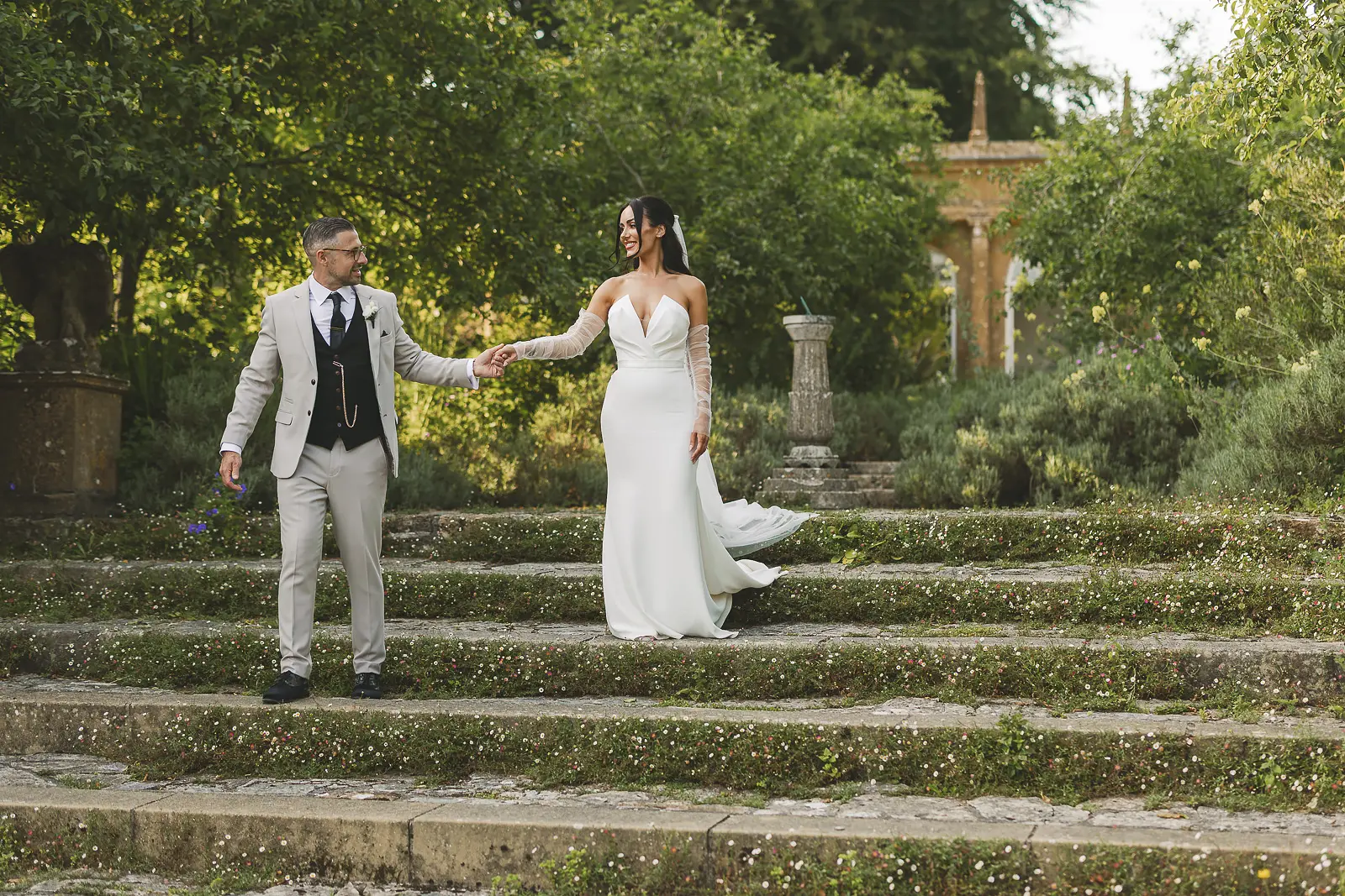 Bride and groom walking together down terraced garden steps at Mapperton, stone walls and green planting surrounding them