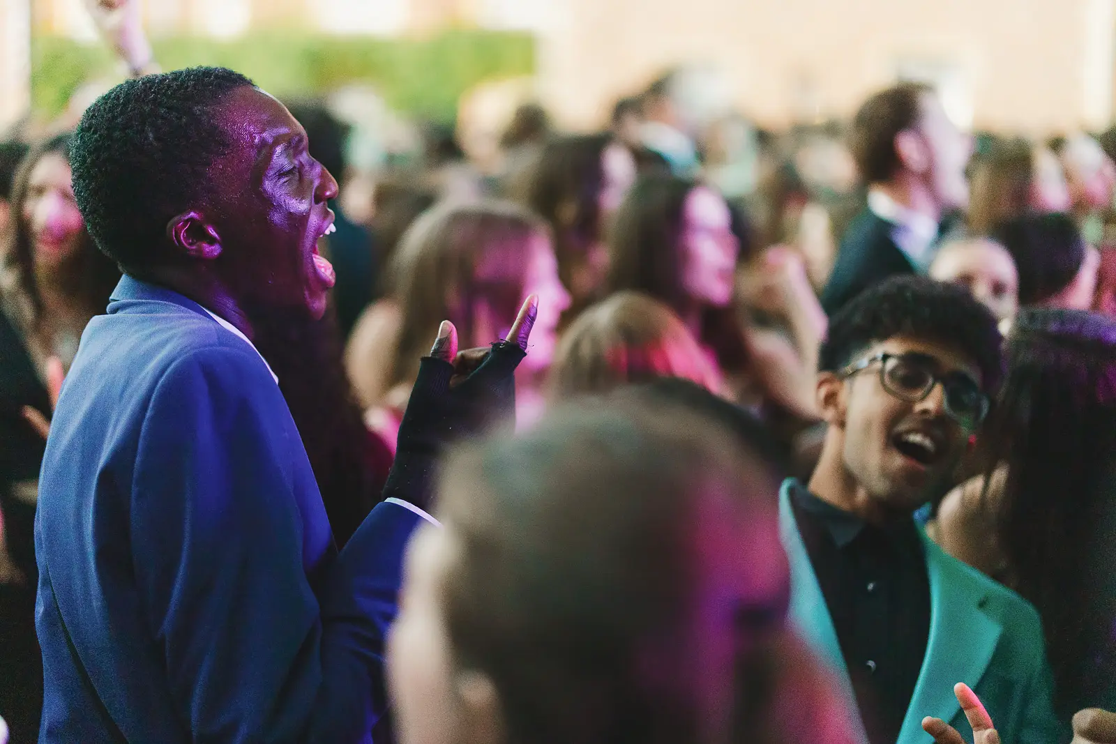 Guest singing with head thrown back in a crowd under pink and purple stage lighting at a large-scale summer ball