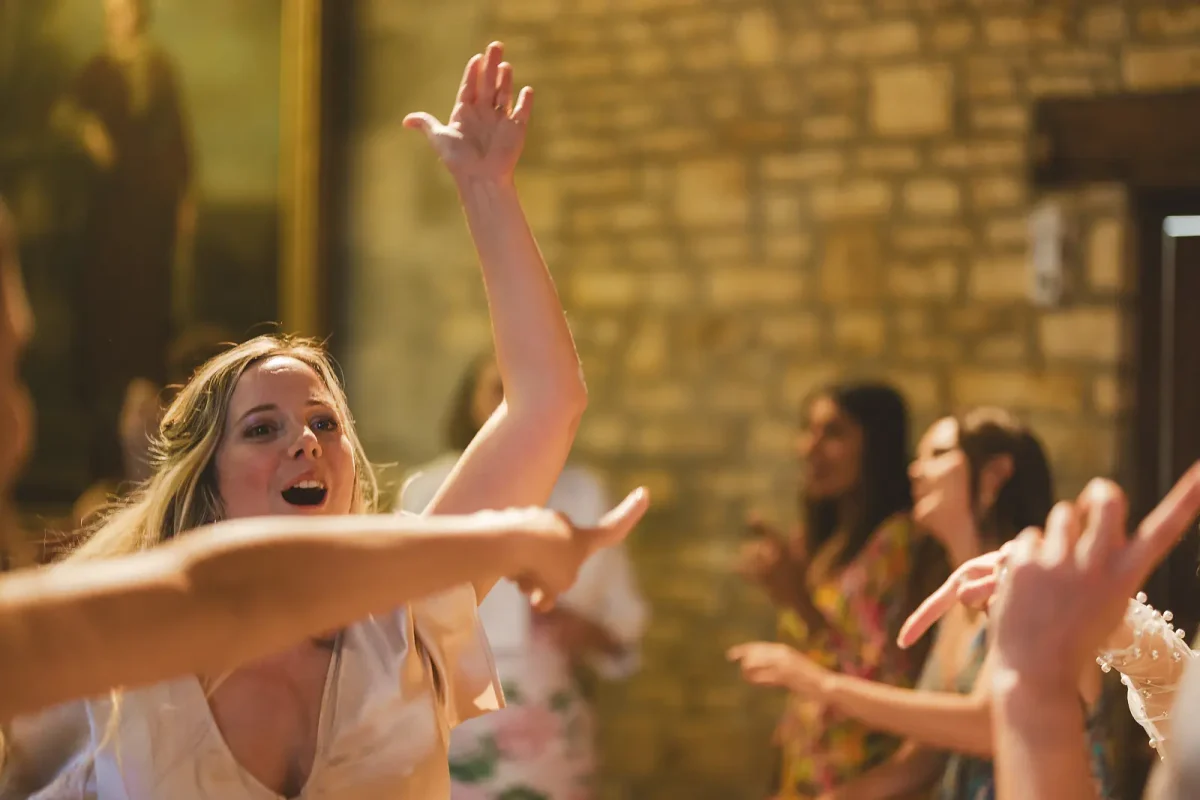 Female wedding guest with arm raised singing along while dancing at the lively evening reception in the tithe barn at Hinton St Mary Estate