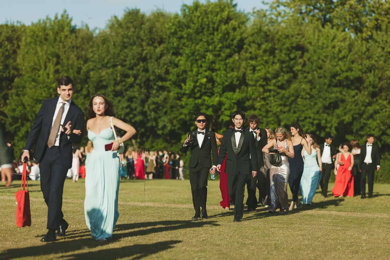 Formal-dressed guests streaming across sunlit lawns as the crowd builds at a Cambridge May Ball