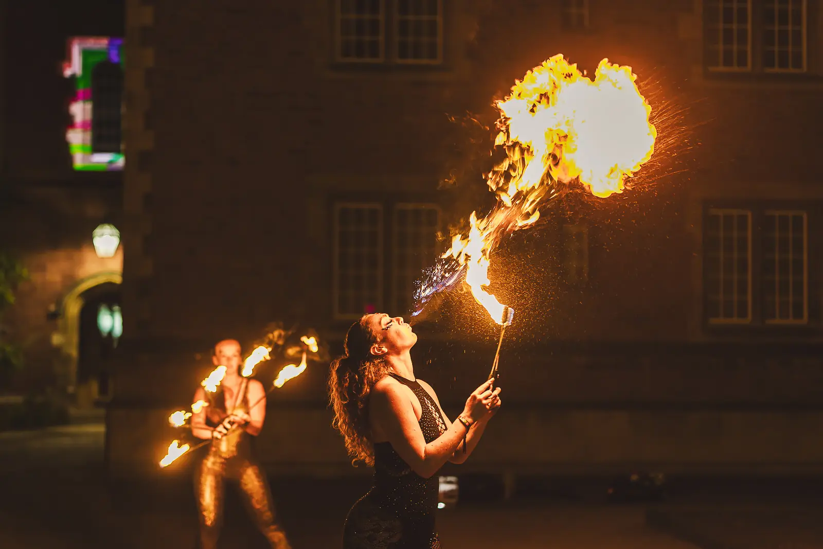 Fire performer breathing a large flame in front of the college building at night at a large-scale summer ball event