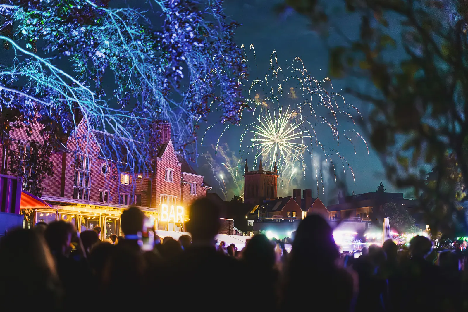 Fireworks bursting above the college rooftops at midnight with the crowd watching from the grounds of a Cambridge summer ball