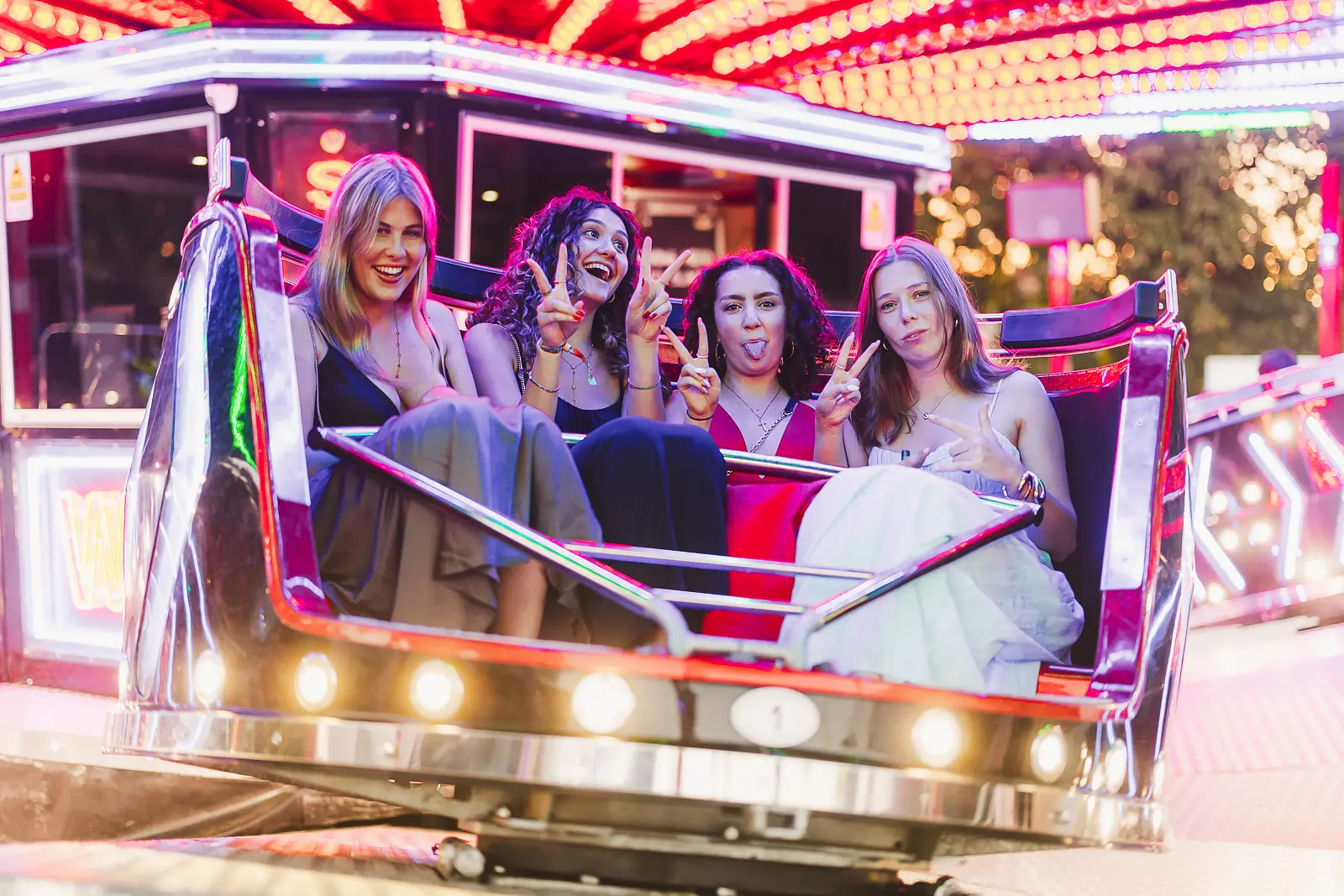Four guests in formal wear laughing on a fairground ride under neon lights at a May Ball event