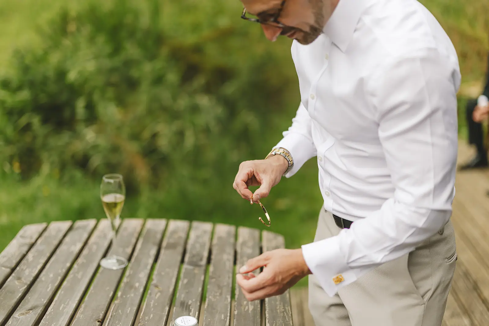 Groom examining a gold ring on an outdoor table during getting ready, part of a wedding morning gift or detail shot