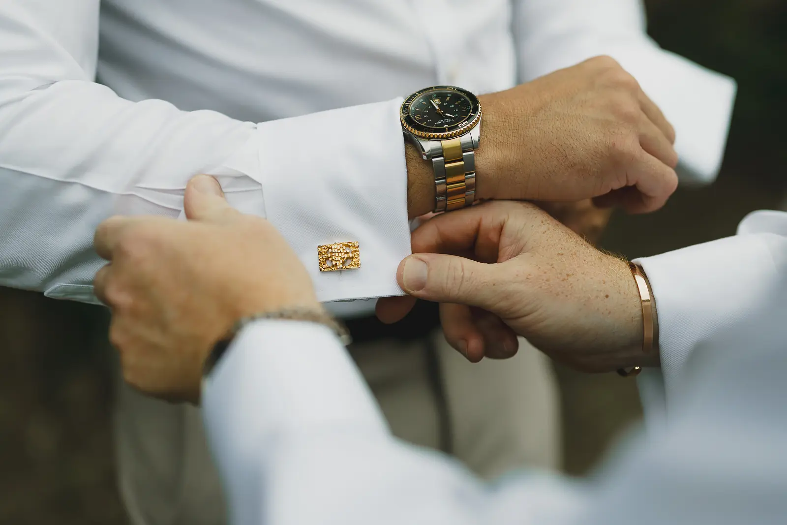Close-up detail of gold cufflink being fastened on the groom's white shirt cuff on the wedding morning