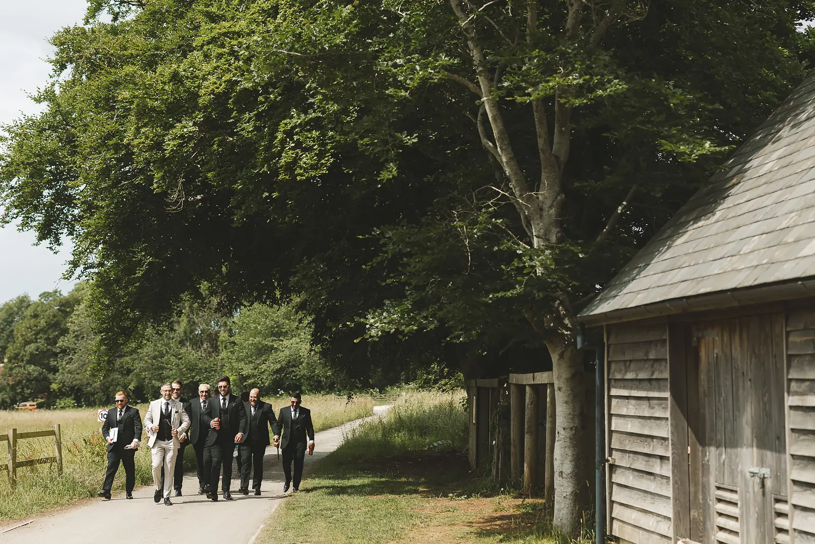 Groom and groomsmen walking in a line along a tree-lined path at Mapperton, suited and ready for the ceremony