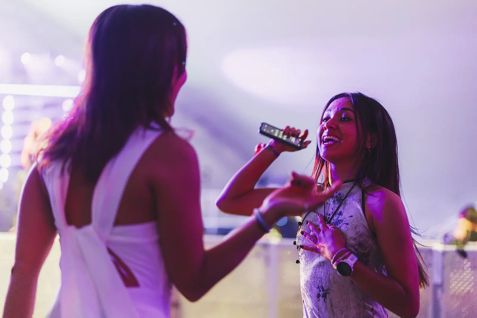 Guest with face glitter singing into a microphone under purple stage lighting at a summer ball event