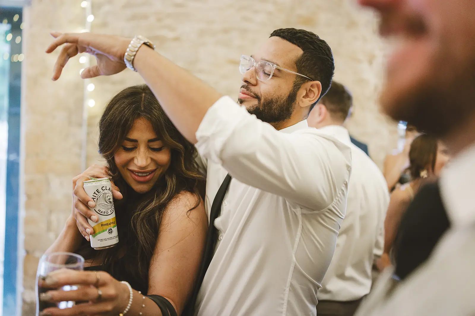 Guests spinning and dancing energetically in the stone barn at the evening reception, fairy lights and stone walls behind