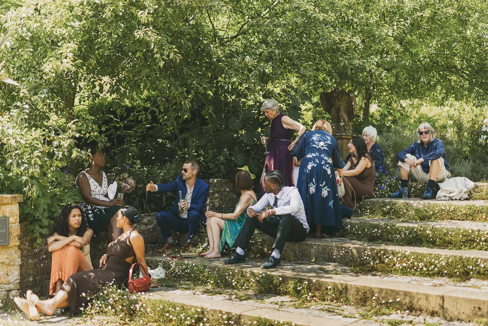 Wedding guests relaxing on the stone garden steps at Mapperton in the summer sunshine during the drinks reception