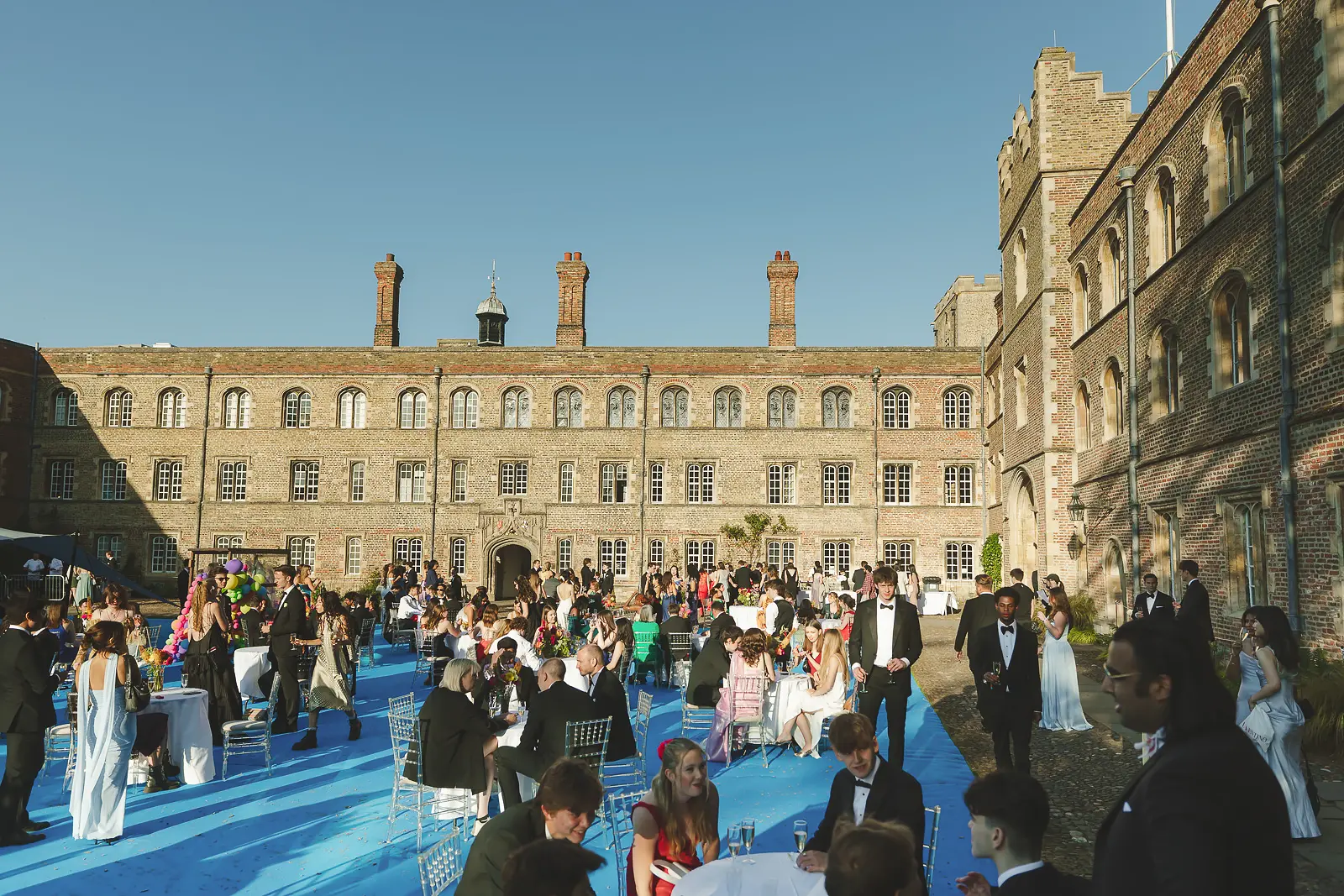Guests mingling in the historic courtyard of Jesus College Cambridge during the May Ball with Georgian brick facade behind