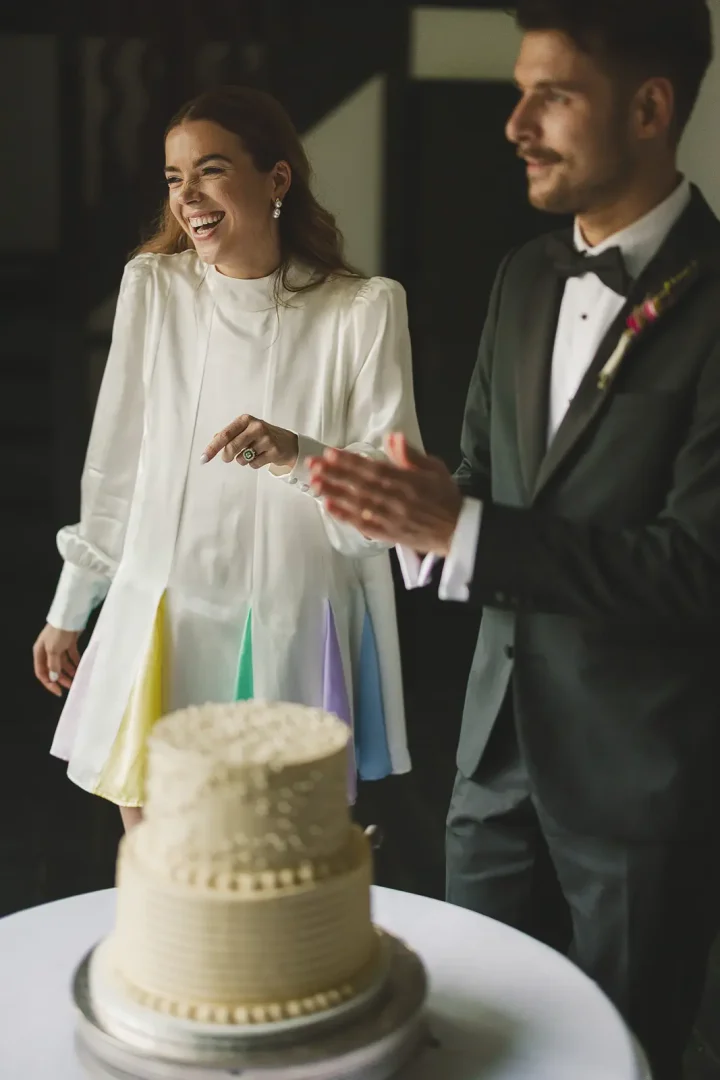 Bride laughing beside wedding cake in Oliver Rubin Dora reception dress at Larmer Tree Gardens