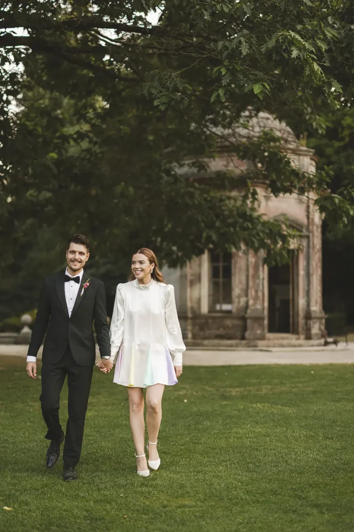 Bride in Oliver Rubin Dora reception dress walking with groom at Larmer Tree Gardens