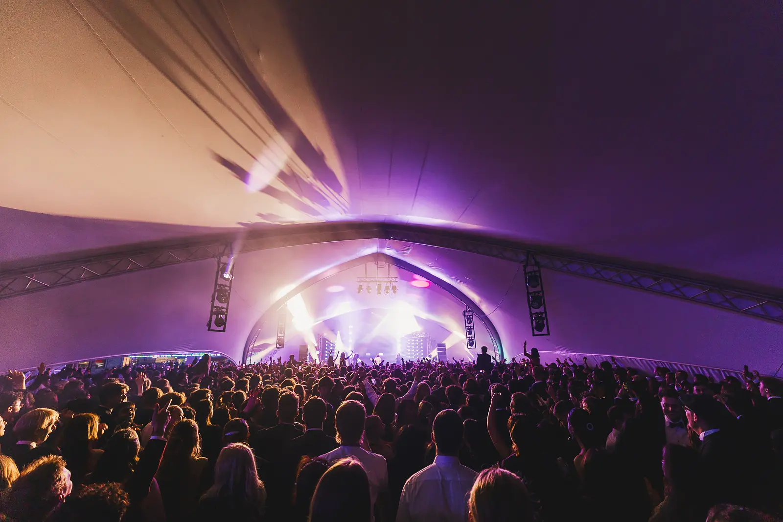 Laser beams cutting through a tent venue above a packed crowd during a late-night May Ball concert performance