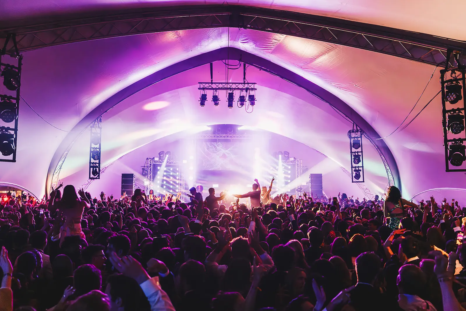 Wide shot of the main tent venue with a band on stage, full production lighting and a packed crowd at a summer ball