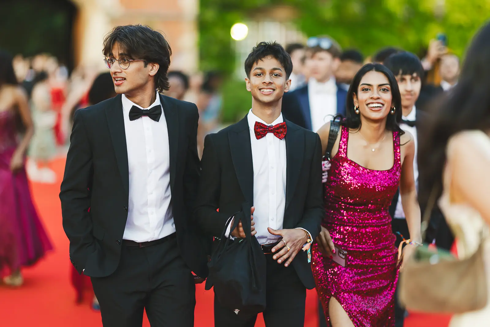 Three friends in black tie and a sequin dress walking the red carpet at a Cambridge summer ball