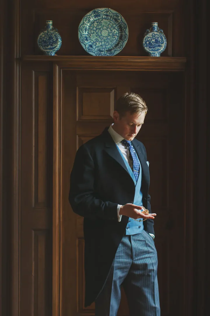 Groom in morning dress checking a pocket watch during preparations inside Smedmore House in Dorset