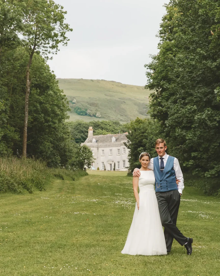 Bride and groom portrait on the tree lined lane leading to Smedmore House with the Purbeck hills behind