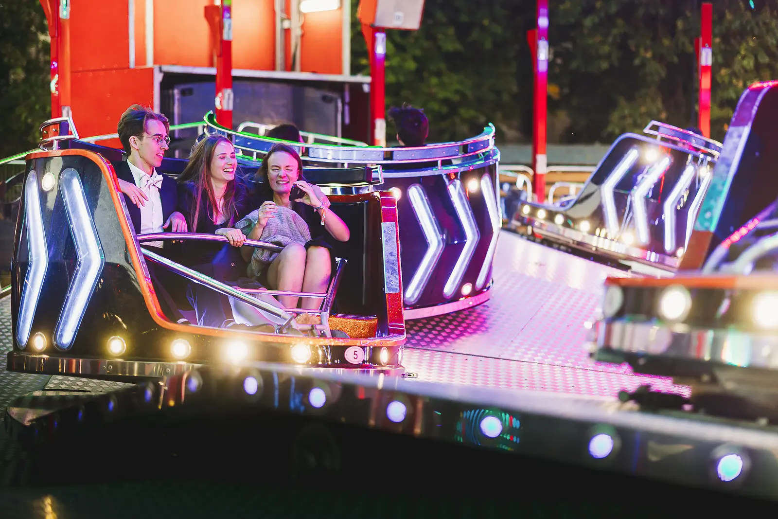 Couple enjoying a spinning fairground attraction lit up with LED lights at a large-scale summer ball event