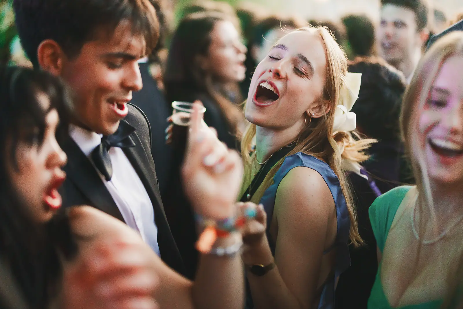 Guests in evening wear singing and dancing uninhibited in a crowd at a large-scale summer ball