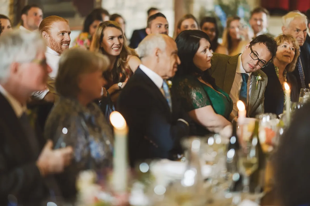 Wedding guests reacting with laughter and emotion at the candlelit tables during the speeches in the tithe barn at Hinton St Mary Estate