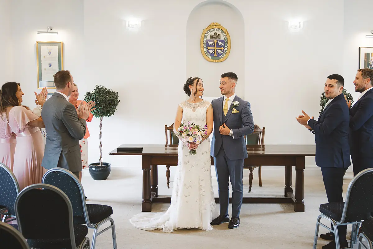 Bride and groom standing together during their wedding ceremony at Wimborne Town Hall register office with guests applauding