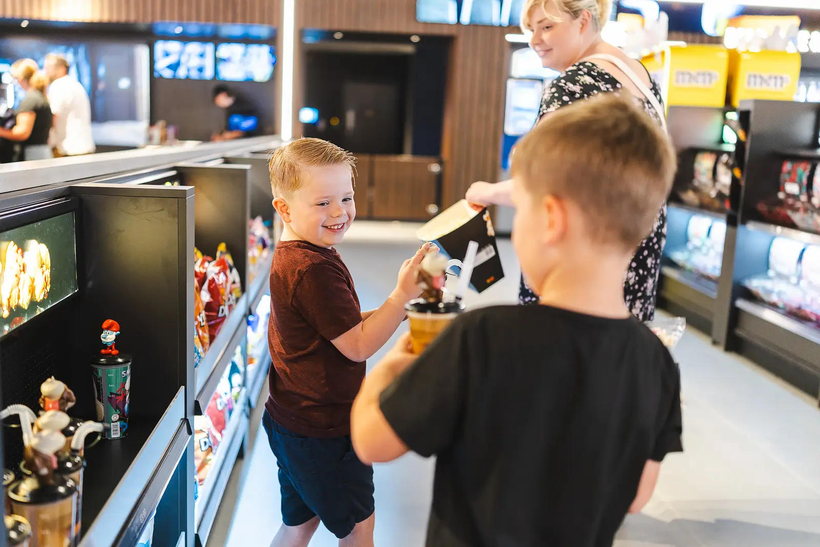 Two boys laughing and sharing snacks at an indoor retail concessions area during a family event in Poole