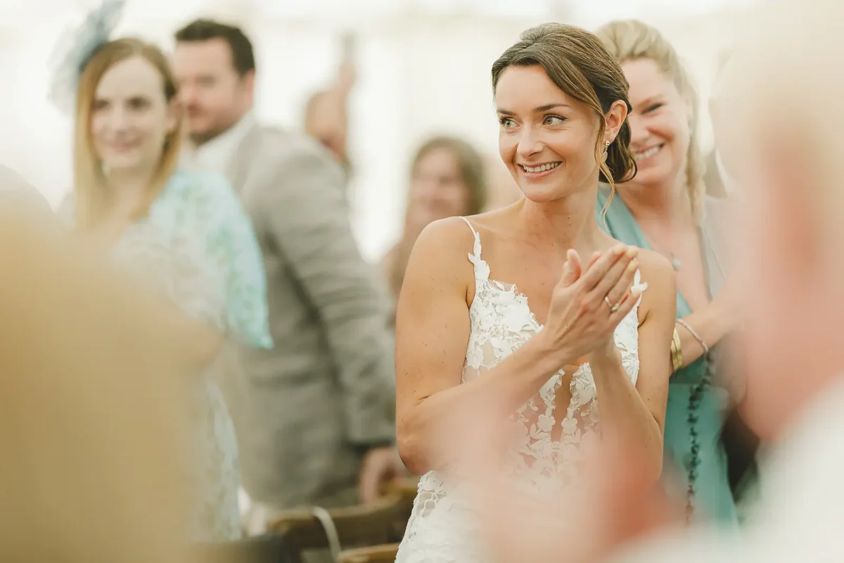 Bride in lace gown clapping and smiling warmly during the wedding reception, bridesmaids behind her