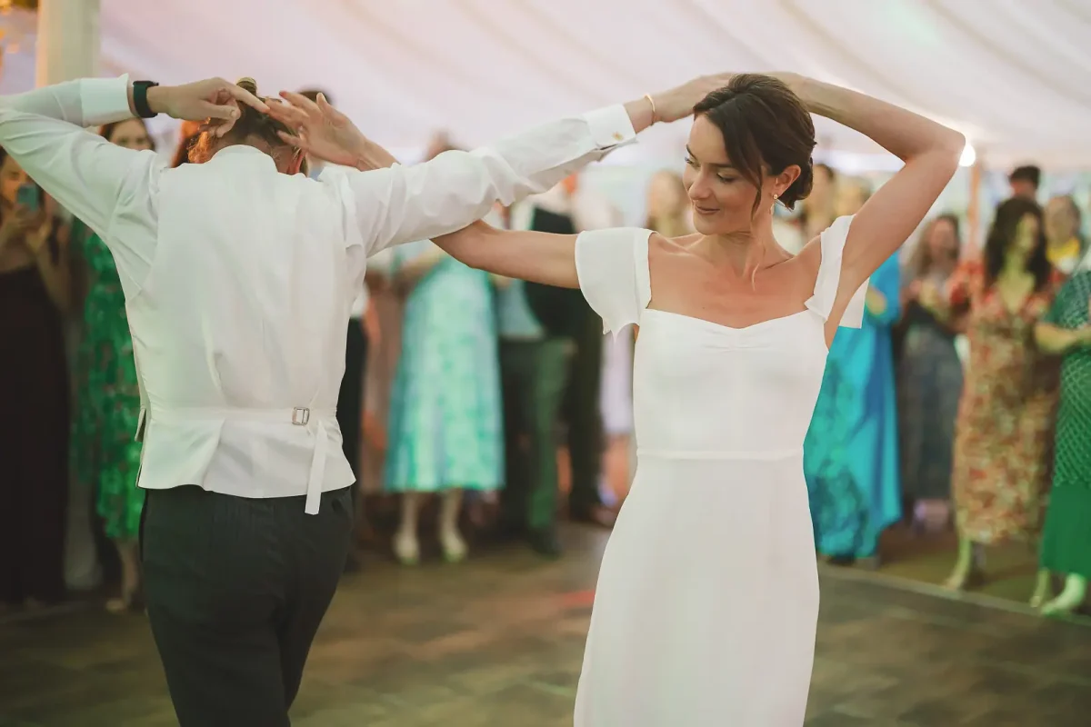Bride and groom spinning together arms raised during their first dance at the marquee evening reception