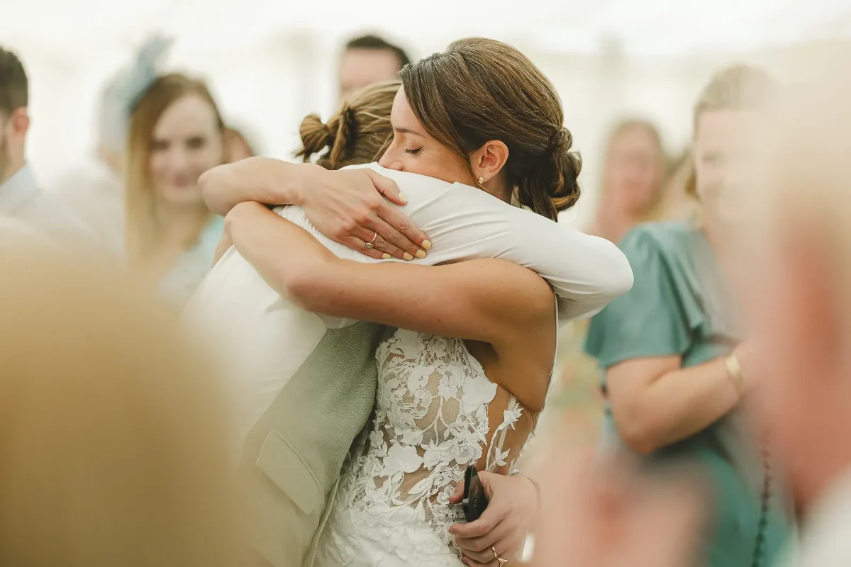 Bride in lace gown embracing a guest warmly after the speeches at a summer marquee wedding reception