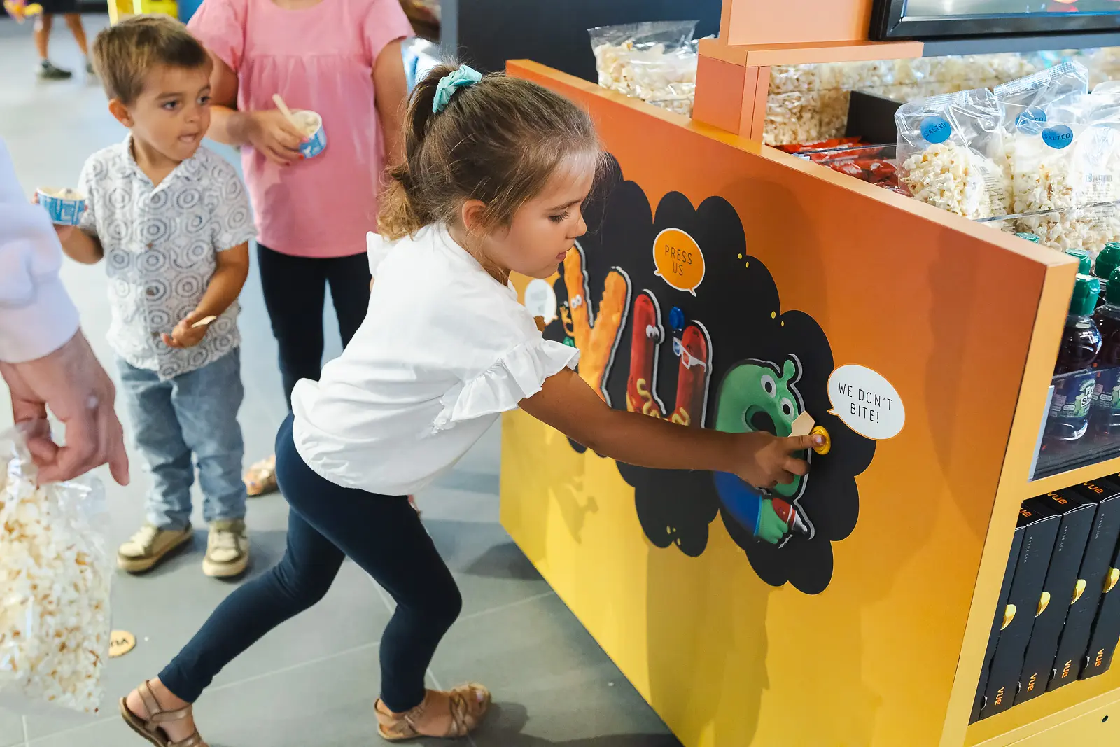 Young girl pressing an interactive branded panel at an indoor commercial event in Poole, with a popcorn counter visible behind her