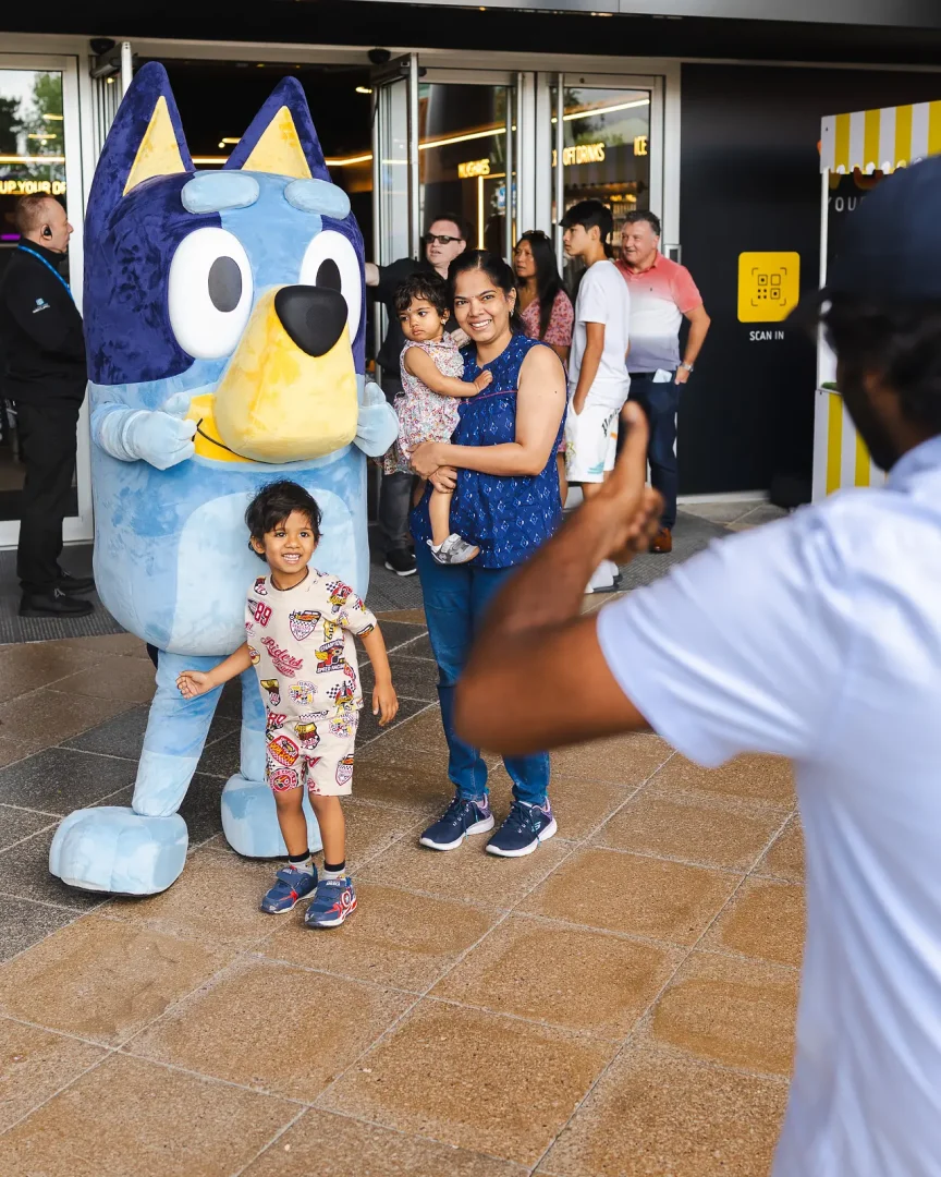 Mother with two young children posing beside a costumed character at a public brand event in Poole while a family member photographs them