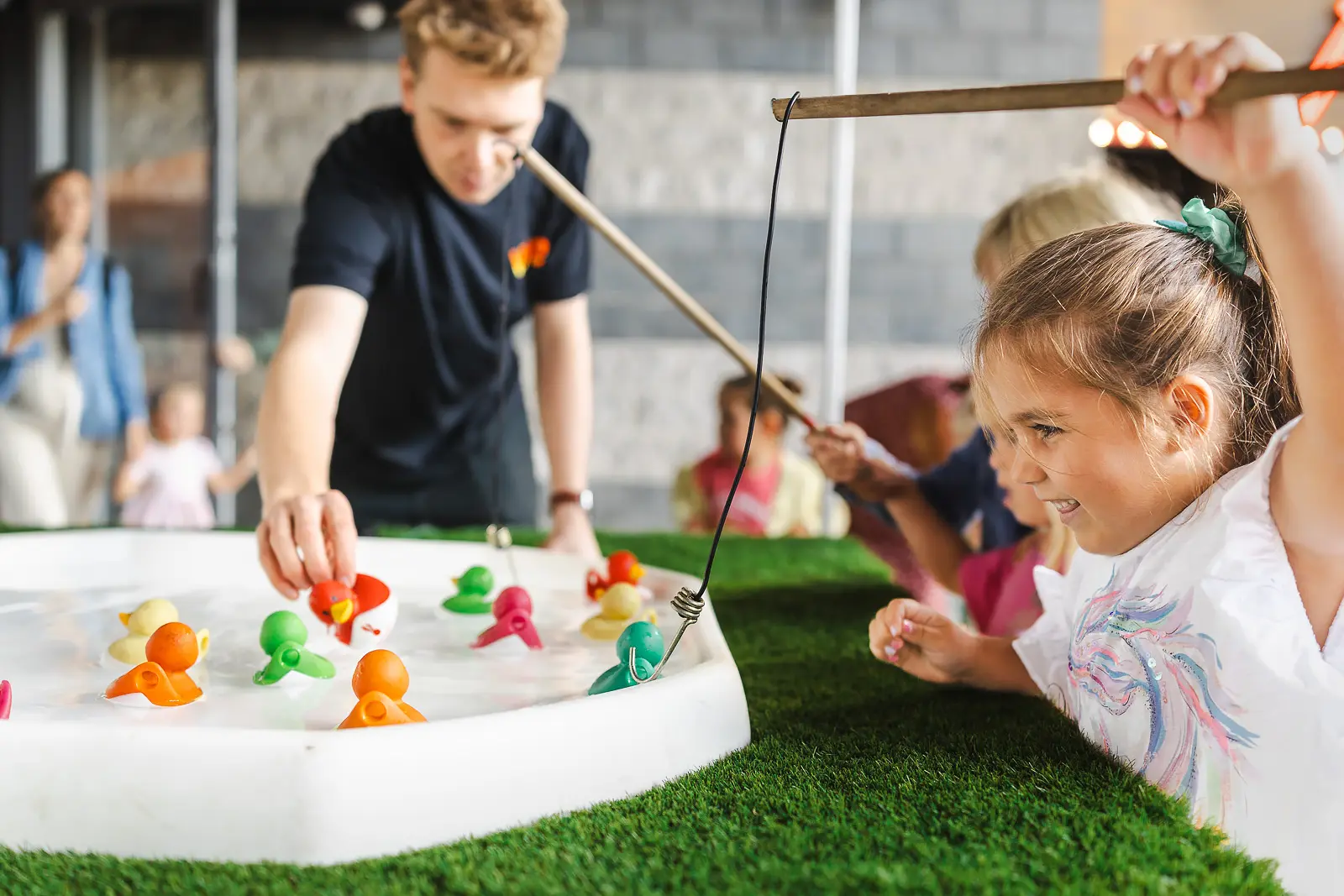 Young girl leaning over a duck pond game at a public event in Poole with event staff guiding the activity