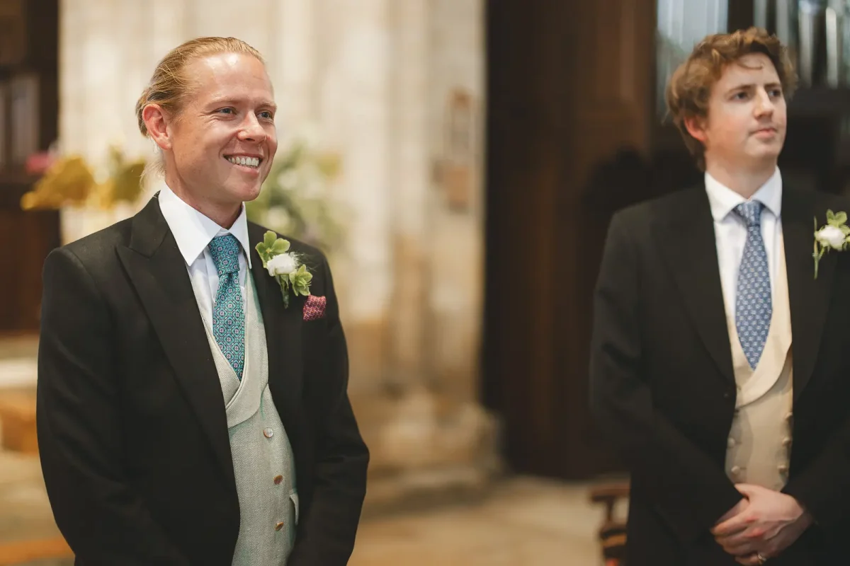 Groom beaming with joy as he sees his bride walking down the aisle at Wimborne Minster church