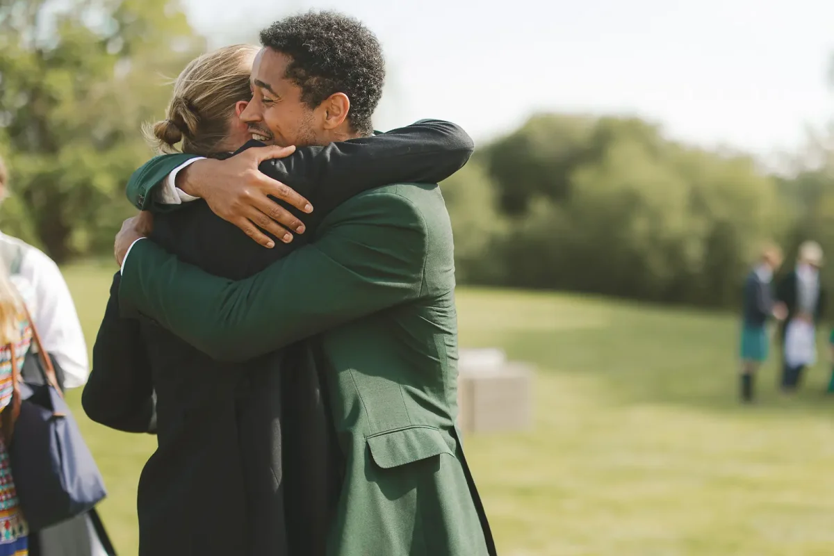 Groom sharing a warm hug with a friend on the sunny lawn at the outdoor summer wedding reception