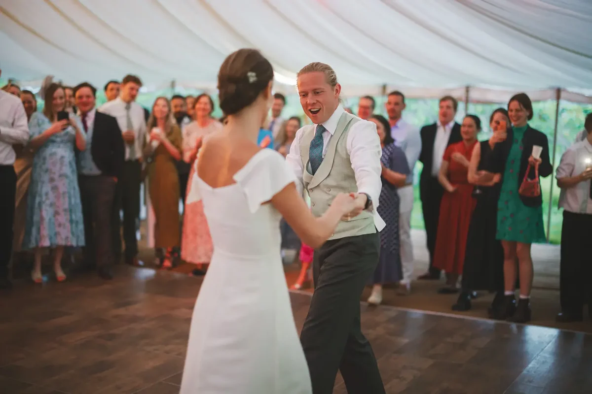Groom laughing joyfully during the first dance as guests cheer and watch inside the Dorset marquee