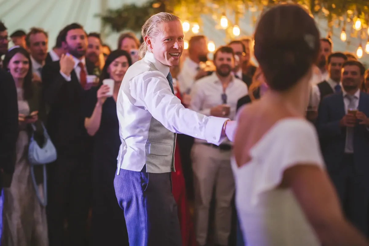 Groom smiling at bride on the dance floor as guests watch the first dance at the marquee wedding reception
