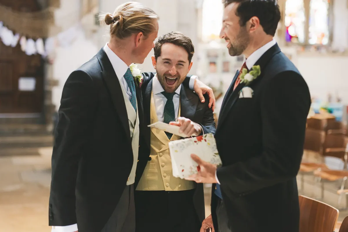 Groomsmen in morning suits laughing together inside Wimborne Minster church before the wedding ceremony
