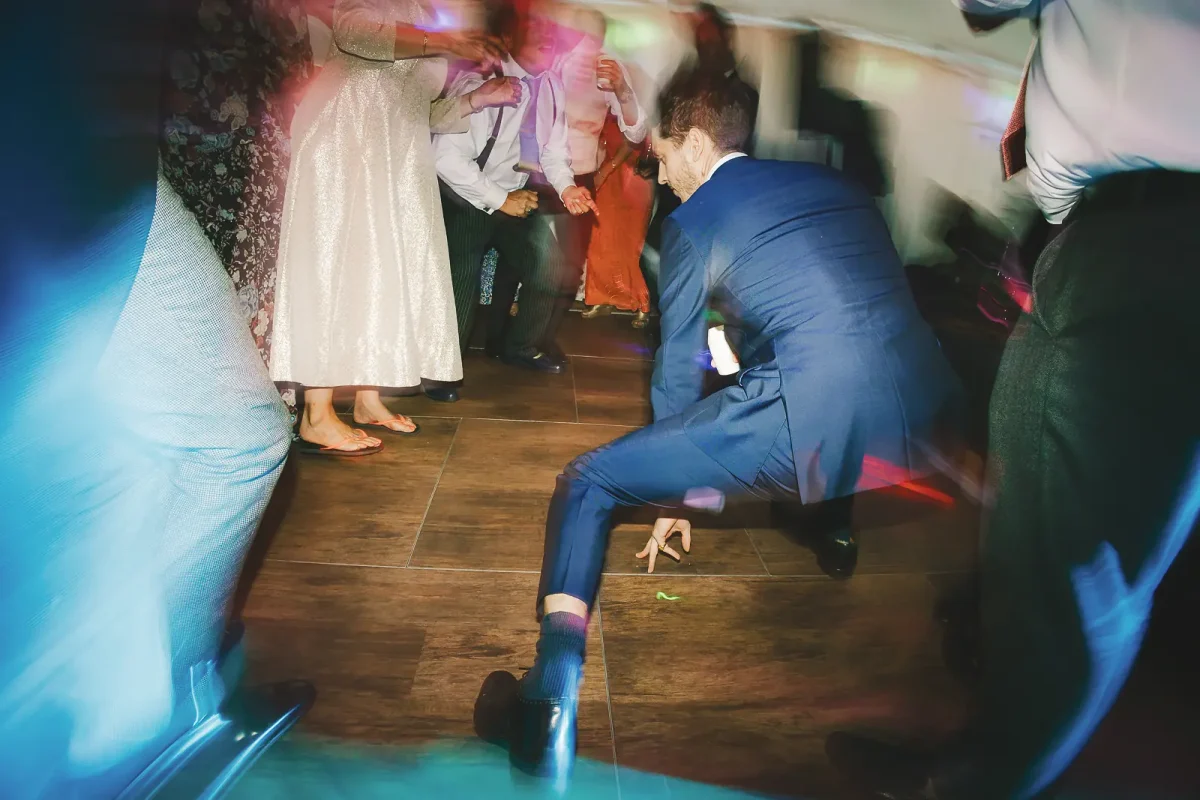 Wedding guest pulling a low move on the dance floor surrounded by feet and coloured lights at the evening party