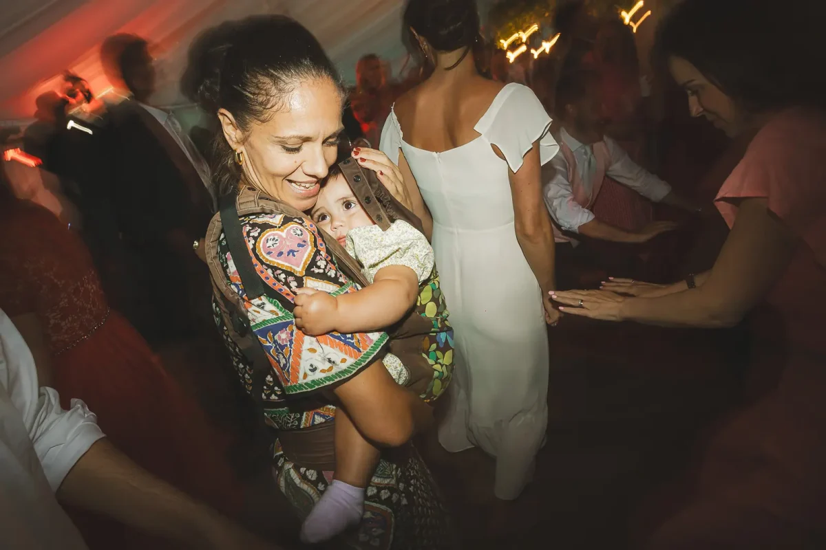 Wedding guest dancing with a baby in a carrier on the marquee dance floor during the evening party
