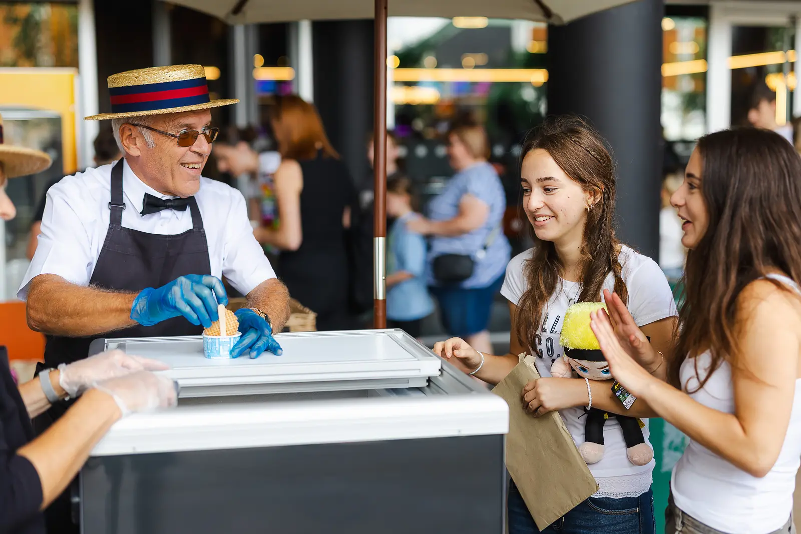Ice cream vendor in a straw boater hat serving two smiling teenagers at an outdoor summer event in Poole