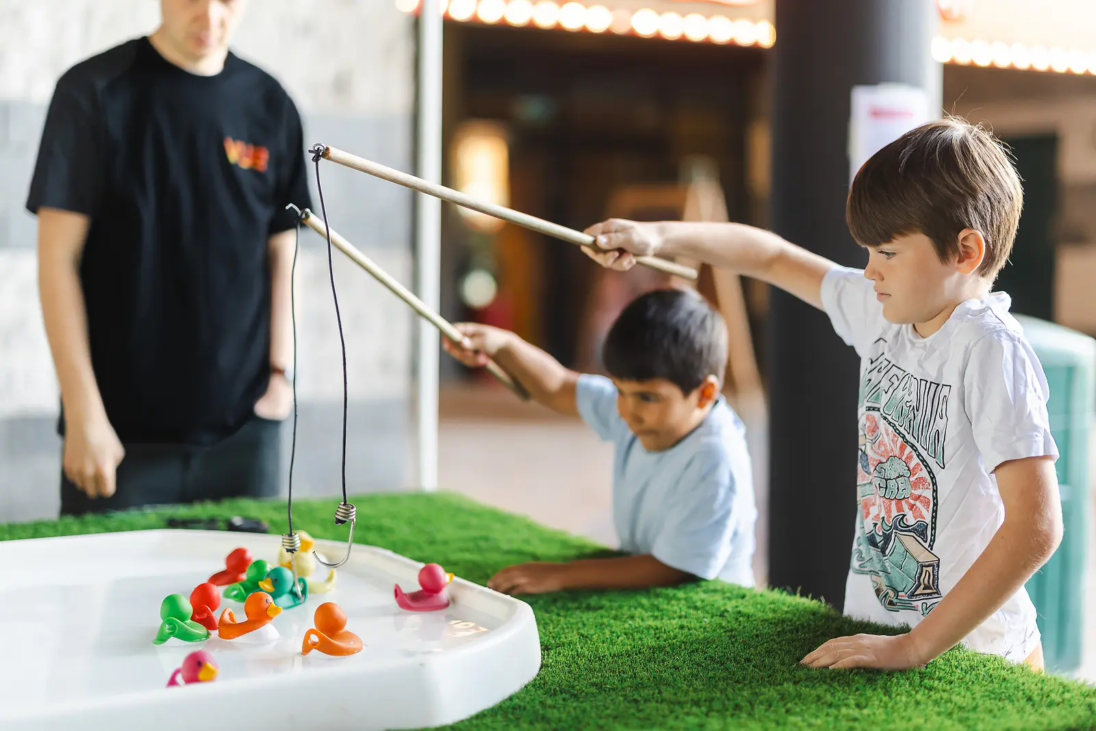 Two boys playing an interactive fishing game at a commercial event in Poole, with event staff in the background