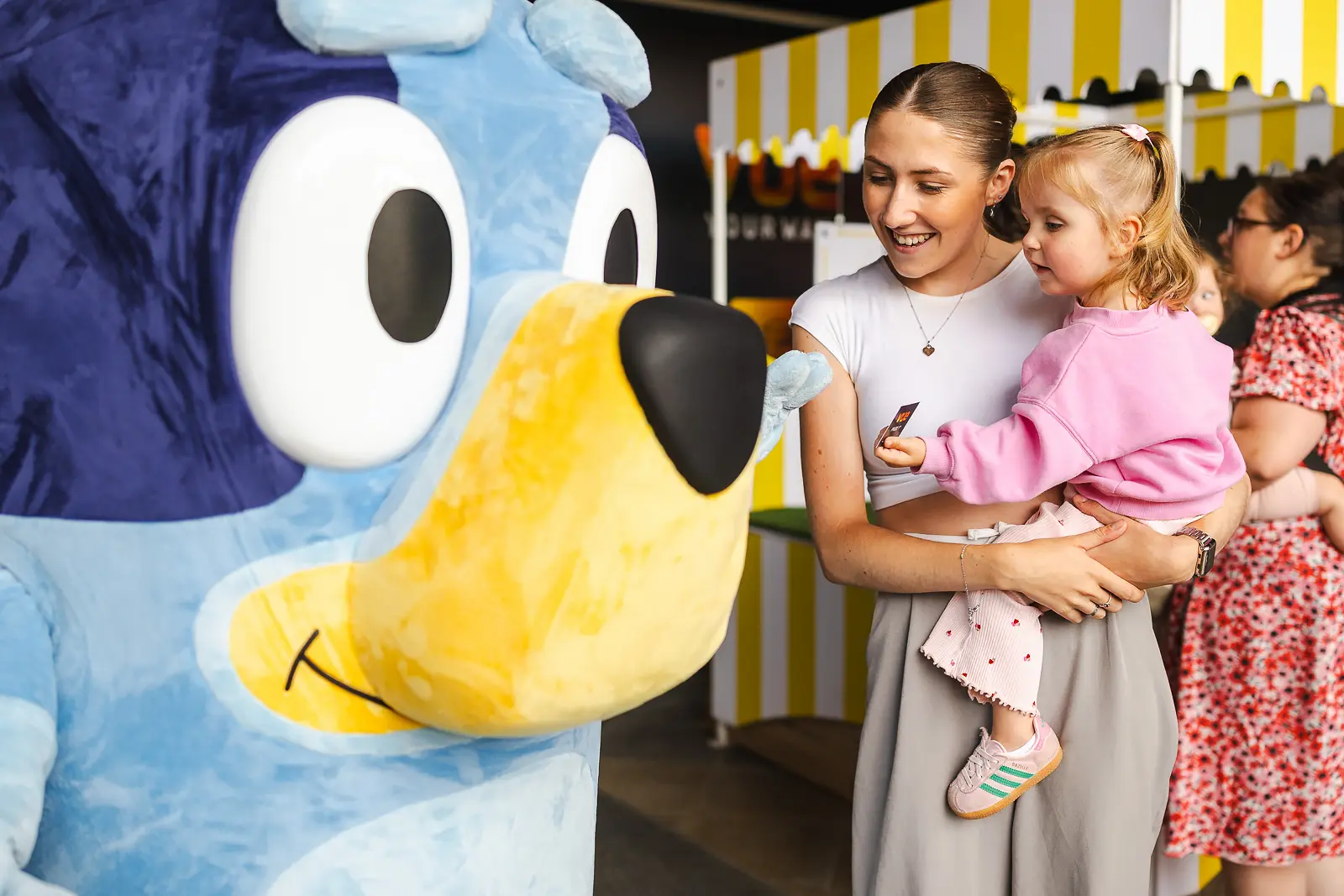 Laughing mother holding her smiling toddler during a costumed character meet and greet at a family brand event in Poole