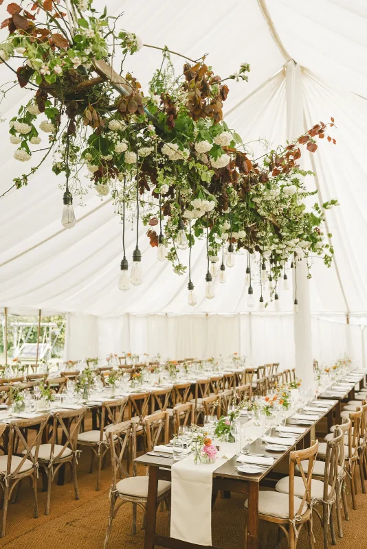 Close view of lush hanging floral installation with roses and trailing greenery above marquee reception tables